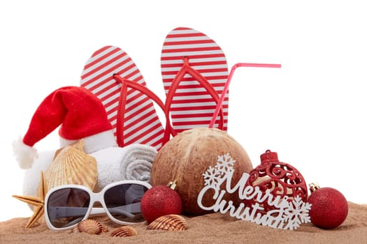 Still life with beach accessories (flip flops, towel, seashells, sand, coconut) and christmas ornaments on white background. Christmas. Winter vacation in warm countries, beach holiday