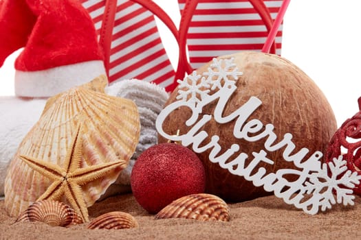 Still life with beach accessories (flip flops, towel, seashells, sand, coconut) and christmas ornaments on white background. Christmas. Winter vacation in warm countries, beach holiday