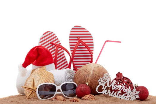 Still life with beach accessories (flip flops, towel, seashells, sand, coconut) and christmas ornaments on white background. Christmas. Winter vacation in warm countries, beach holiday