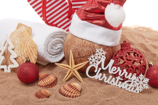 Still life with beach accessories (flip flops, towel, seashells, sand, coconut) and christmas ornaments on white background. Christmas. Winter vacation in warm countries, beach holiday