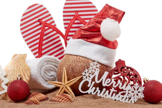 Still life with beach accessories (flip flops, towel, seashells, sand, coconut) and christmas ornaments on white background. Christmas. Winter vacation in warm countries, beach holiday