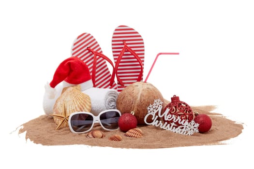 Still life with beach accessories (flip flops, towel, seashells, sand, coconut) and christmas ornaments on white background. Christmas. Winter vacation in warm countries, beach holiday