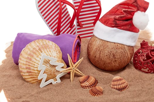 Still life with beach accessories (flip flops, towel, seashells, sand, coconut) and christmas ornaments on white background. New Year and Christmas. Winter vacation in warm countries, beach holiday