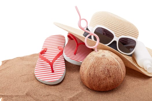 Beach accessories: flip flops, straw hat, sunglasses, sunscreen and coconut, lying on the sand on white background. Concept of sea vacation and travel. Summer background, Protection from uv
