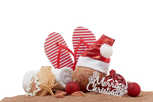 Still life with beach accessories (flip flops, towel, seashells, sand, coconut) and christmas ornaments on white background. Christmas. Winter vacation in warm countries, beach holiday