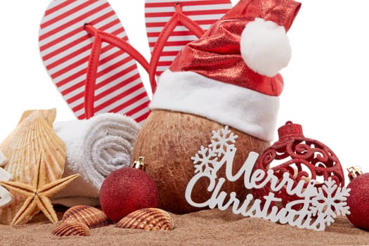 Still life with beach accessories (flip flops, towel, seashells, sand, coconut) and christmas ornaments on white background. Christmas. Winter vacation in warm countries, beach holiday