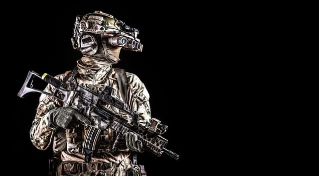 Half length portrait of army special forces rifleman, commando elite soldier equipped radio tactical headset, armed service rifle, using night vision goggles in darkness, isolated on black, copyspace
