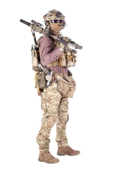 Strikeball enthusiast in checkered shirt wearing military ammunition, face mask, helmet and radio headset, tactical glasses, camo pants, armed service rifle and handgun studio shoot isolated on white