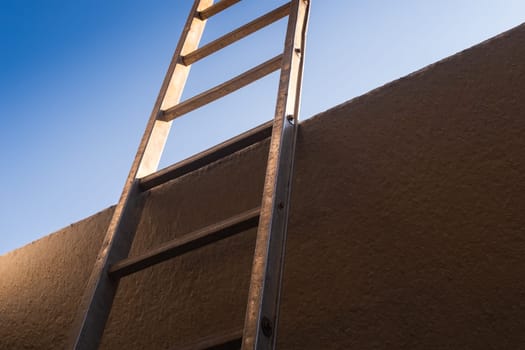 Low angle view of metal ladder leaning against concrete wall, the background is a clear sky. Conceptual themes of overcoming obstacles, challenges and new opportunities.