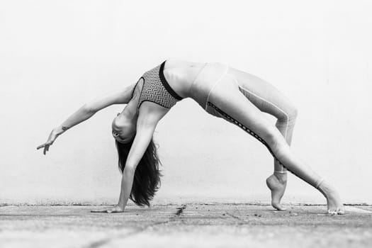 Fit sporty active girl in fashion sportswear doing yoga fitness exercise in front of gray wall, outdoor sports, urban style. Black and white image.