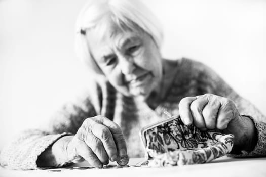 Concerned elderly 96 years old woman sitting at table at home and counting remaining coins from pension in her wallet after paying bills. Unsustainability of social transfers and pension system.