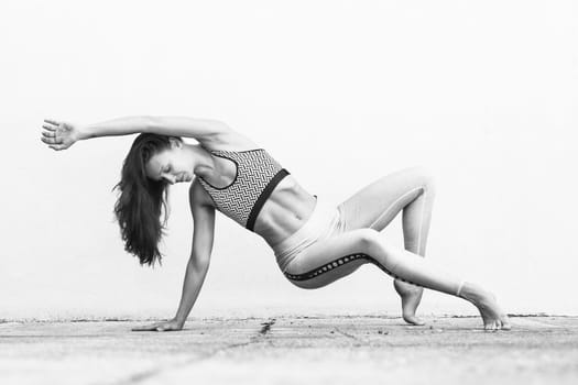 Fit sporty active girl in fashion sportswear doing yoga fitness exercise in front of gray wall, outdoor sports, urban style. Black and white image.