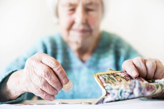 Concerned elderly 96 years old woman sitting at table at home and counting remaining coins from pension in her wallet after paying bills. Unsustainability of social transfers and pension system.