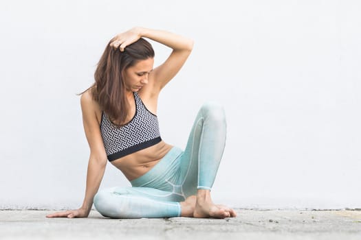 Fit sporty active girl in fashion sportswear sitting on the floor in front of gray wall. Outdoor sports, active urban lifestyle concept.