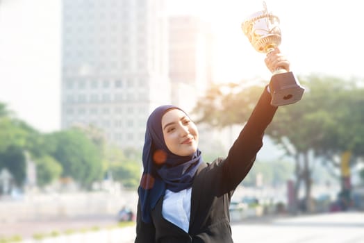 Muslim businesswoman holding a trophy, woman power in business, top performance concept.