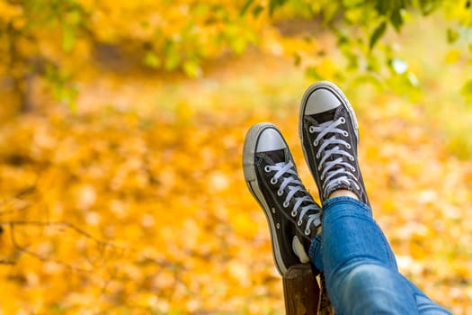 Relaxed teenage girl wearing sneakers is lying on bench in autumn park closeup. Focus on sneakers.