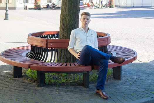 Handsome young man sitting on a bench in the town