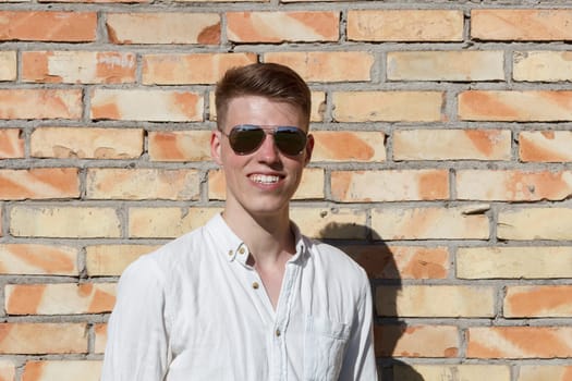 Smiling young man portrait with retro shiny drop sunglasses against brick wall