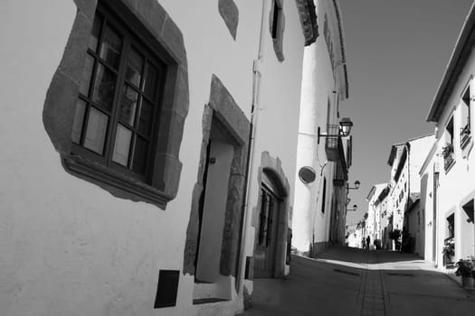 Low angle view of white houses along a narrow street in Begur. Two children walk away in the distance. Black and white wide-angle photo.