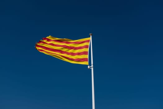 Low angle view at Catalonian flag with torn edges waving over clear sky.