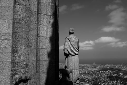 Statue of an Apostle crowing the roof of the Temple Expiatori del Sagrat Cor (Expiatory Church of the Sacred Heart) Beyond the sculpture, enjoyment a breathtaking view of the city of Barcelona.