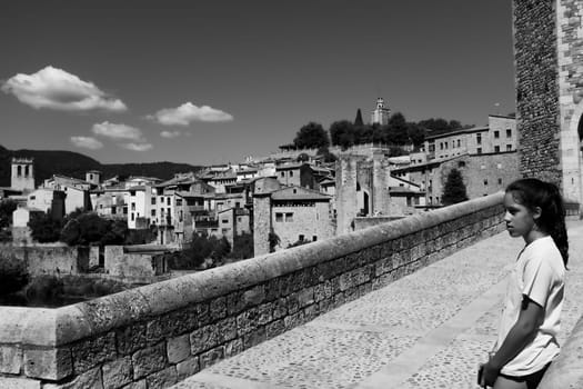 Cute young girl with long hair and a white T-shirt enjoying the view over the medieval village of Besalù.