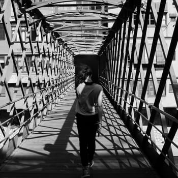 Rear view of a young girl with fluttering hair walking across the Pont de les Peixateries Velles, constructed by G. Eiffel in Gerona, Catalonia, Spain.