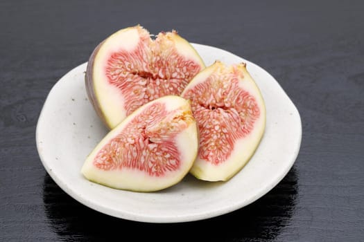 Ripe sweet fig on a plate on black background