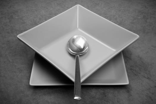 Gray square shape crockery, plates with spoon are on gray background, modern design for restaurants.