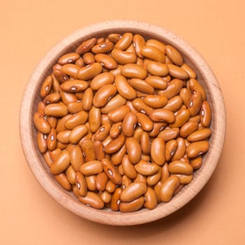 Brown bean seeds are in wooden bowl on beige background, legume as food ingredient.
