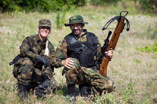 Female and male soldiers in military uniforms are outdoors in nature.