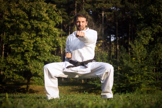 Karateist in white kimono is practicing martial arts in forest in nature on green background.