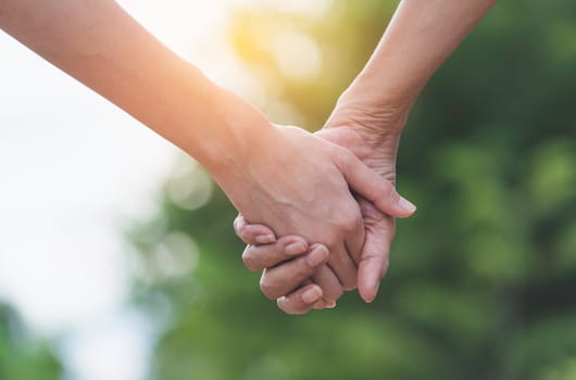 Hand of lady and younger lady holding together on blur background