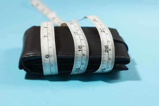 concept of budget and money. Purse is tied with measuring tape on blue background