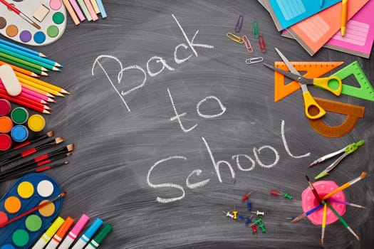 Stationery accessories on background of school blackboard with inscription: Back to school. Top view. School accessories for children's education and development. Office supplies.