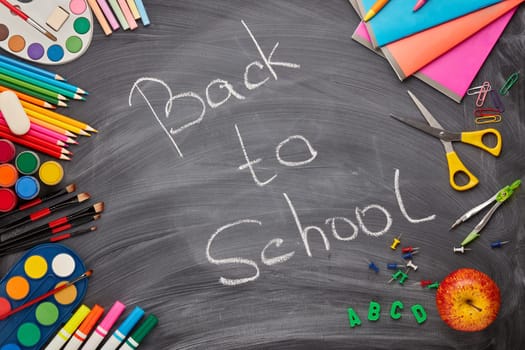 Stationery accessories on background of school blackboard with inscription: Back to school. Top view. School accessories for children's education and development. Office supplies.