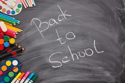 Stationery accessories on background of school blackboard with inscription: Back to school. Top view. School accessories for children's education and development. Art lesson or drawing