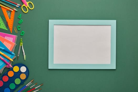 Blue frame with blank sheet and stationery accessories on green background. Top view, copy space. School accessories for education and development. Office supplies