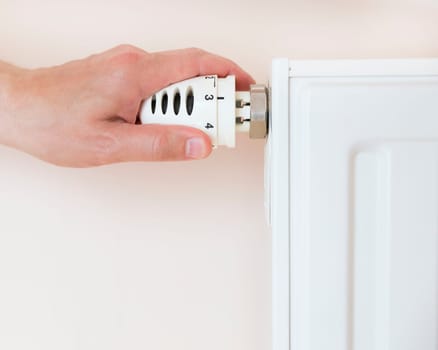 Hand adjusting thermostat valve of heating radiator in a room.