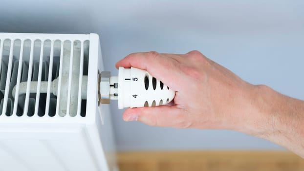 Hand adjusting thermostat valve of heating radiator in a room.