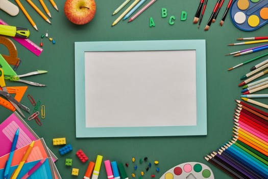 Blue frame with blank sheet and stationery accessories on green background. Top view, copy space. School accessories for education and development. Office supplies