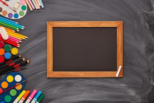 Blank black board and stationery accessories on background of school blackboard. Top view, copy space. School accessories for children's education and development. Art lesson or drawing