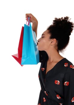 A happy multi-racial woman standing and holding her shopping.bags high up, kissing them, with her curly black.hair, isolated for white background.