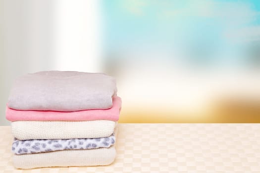 Stack of winter clothes. A pile of colorful cozy warm sweaters on a bright wooden table against abstract blurred natural background. Autumn and winter clothes. Space for display product montage.