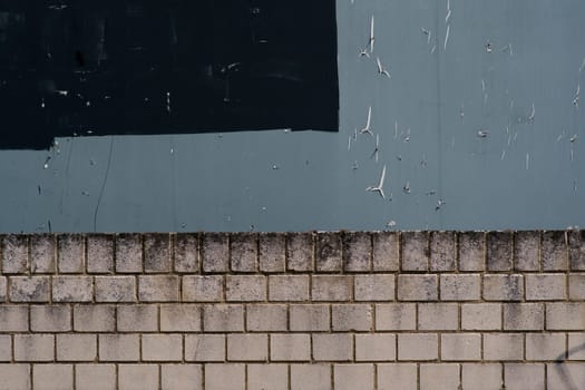 The close-up of a gray billboard with torn pieces of paper over a bright wall edge...