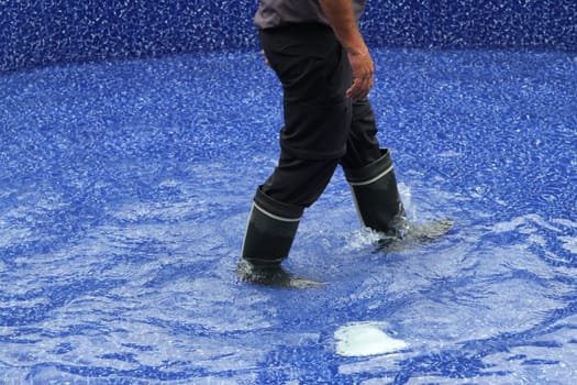 Legs with wading rubber boots walking through water in a pool