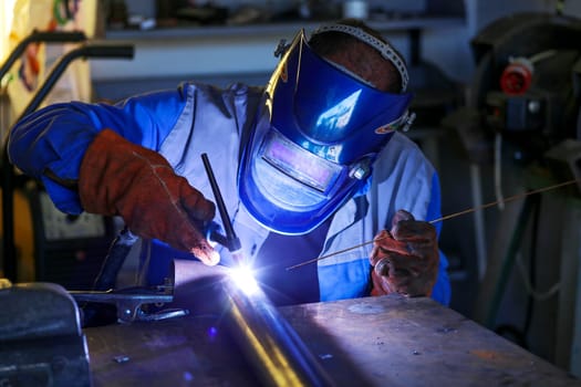 A worker welds a pipe with inert gas in a workshop.