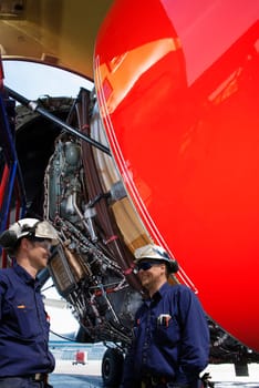 two airplane-mechanics servicing a large jet engine