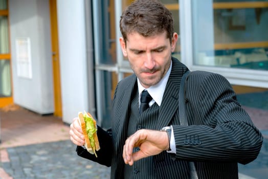 businessman in suit in front of city- background is eating and looking for time