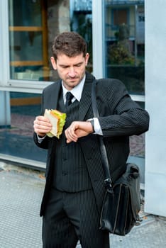 businessman in suit in front of city- background is eating and looking for time
